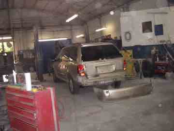 A beige minivan being repaired in a dusty shop
