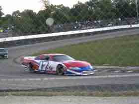 A blurry number 17 stock car photographed through a fence